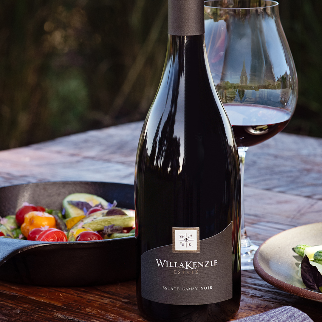 A bottle of WillaKenzie Estate Gamay Noir near plates of food.